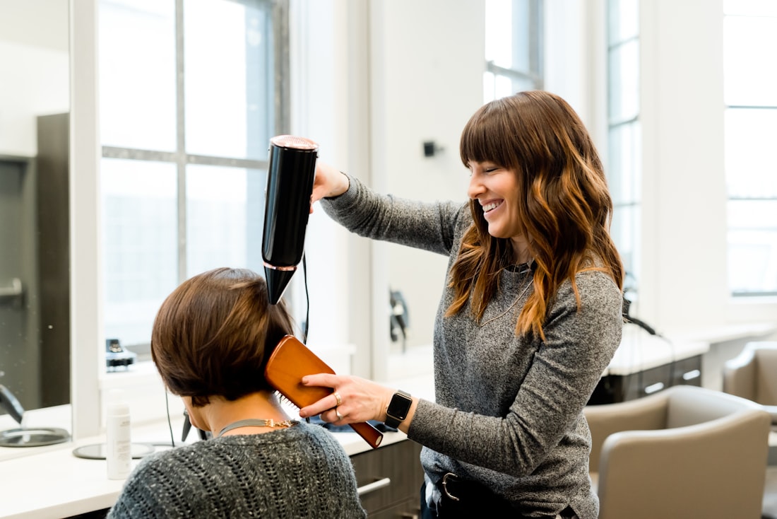 Stylistin föhnt einer Kundin lächelnd die Haare im Salon